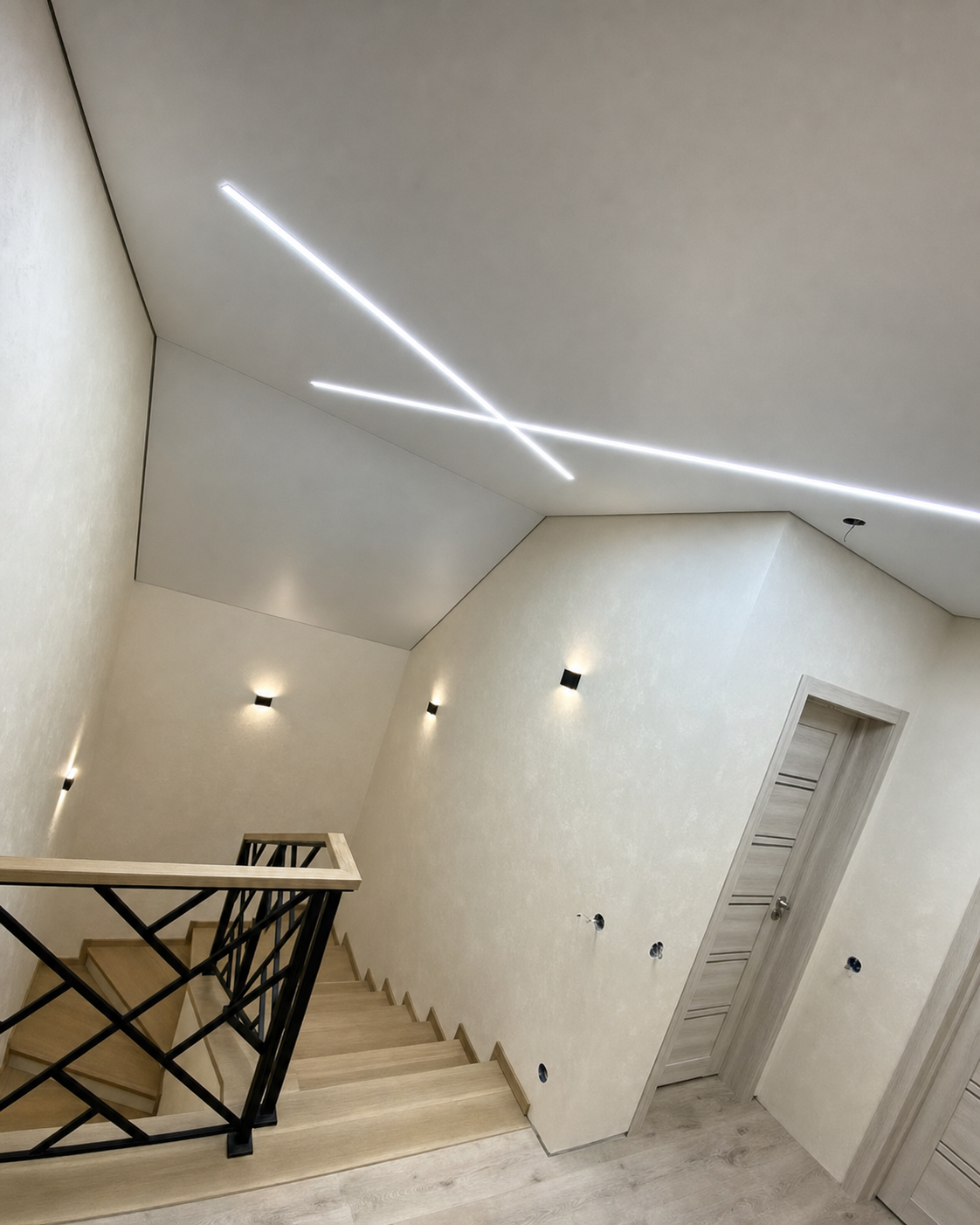 An asymmetric stairwell ceiling crossed by two intersecting light lines