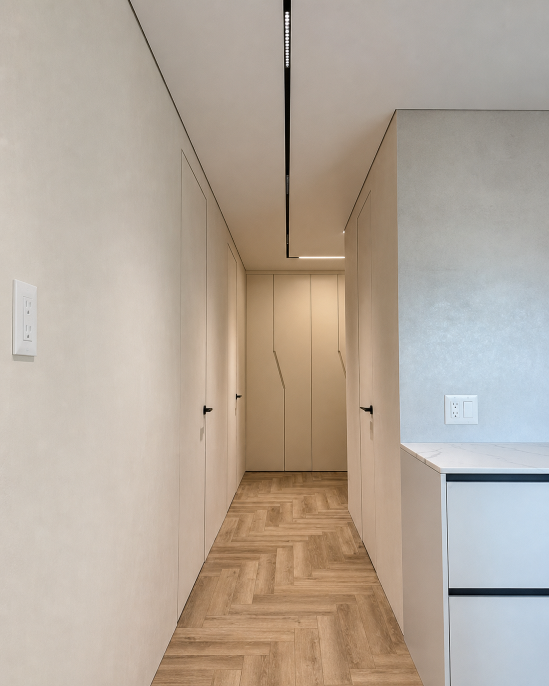 A herringbone-floored hallway lit by a slim ceiling channel
